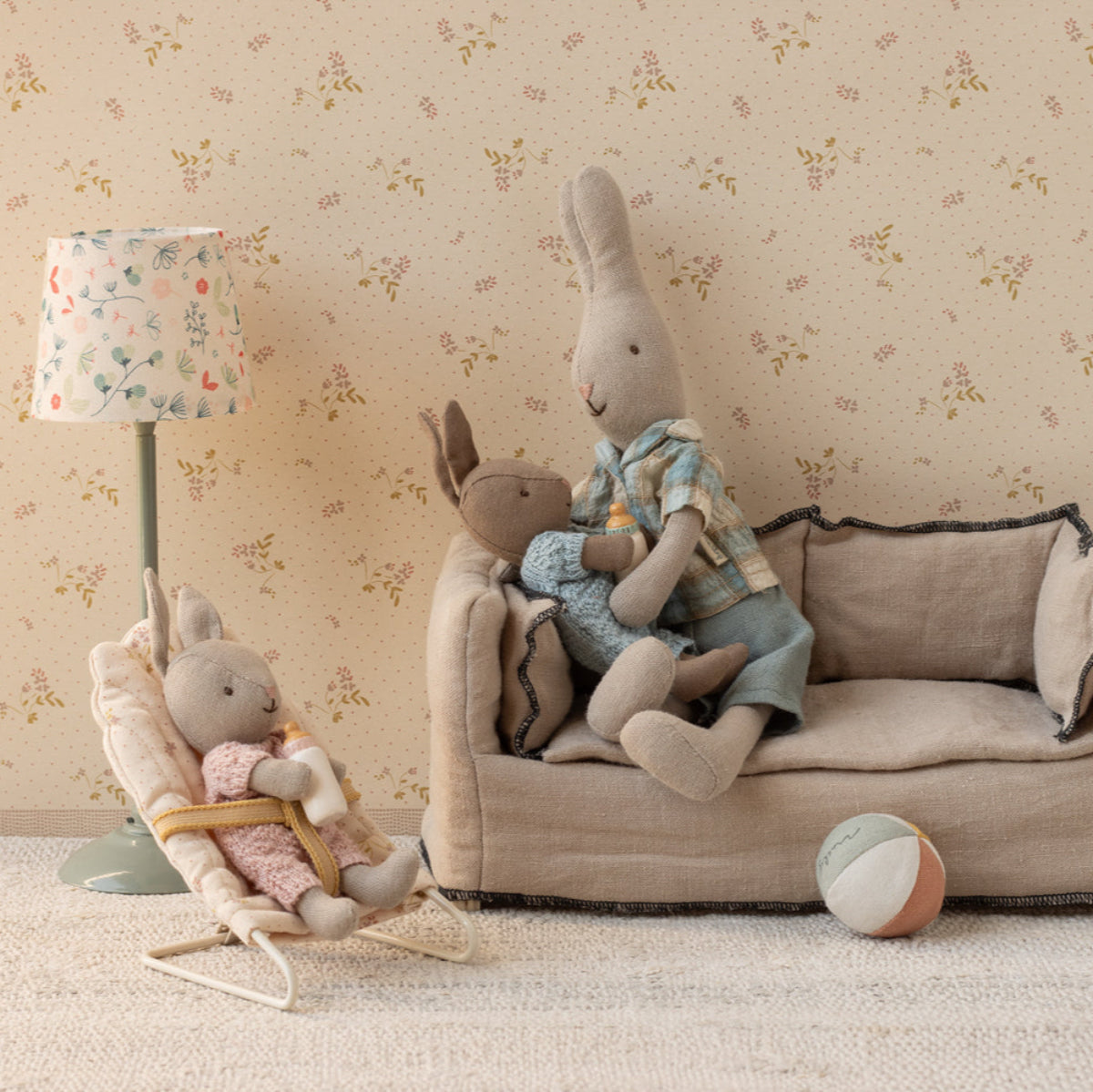Stuffed animals on a small couch and chair against a floral wallpapered wall.
