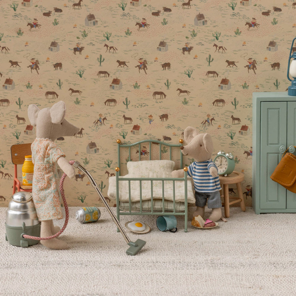 Miniature scene with toy mice in a room setting, including a bed and dresser, with a patterned wallpaper background.
